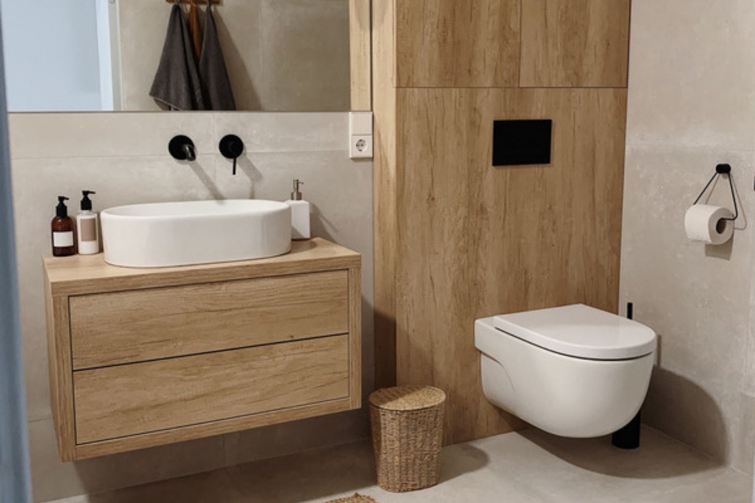 Nordisk badeværelse med svævende vaskemøbel i lyst træ, hvid bowlevask, sort armatur og væghængt toilet foran træpanel