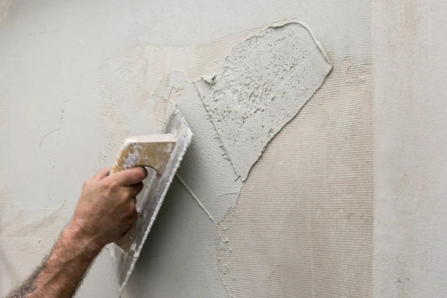 Hånd påfører et lag microcement på en væg med en glittespartel
